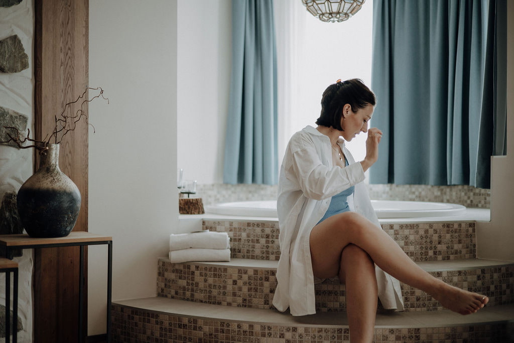 Dame sitzt mit Bademantel bekleidet am Rand der Badewanne in der Hotelsuite.